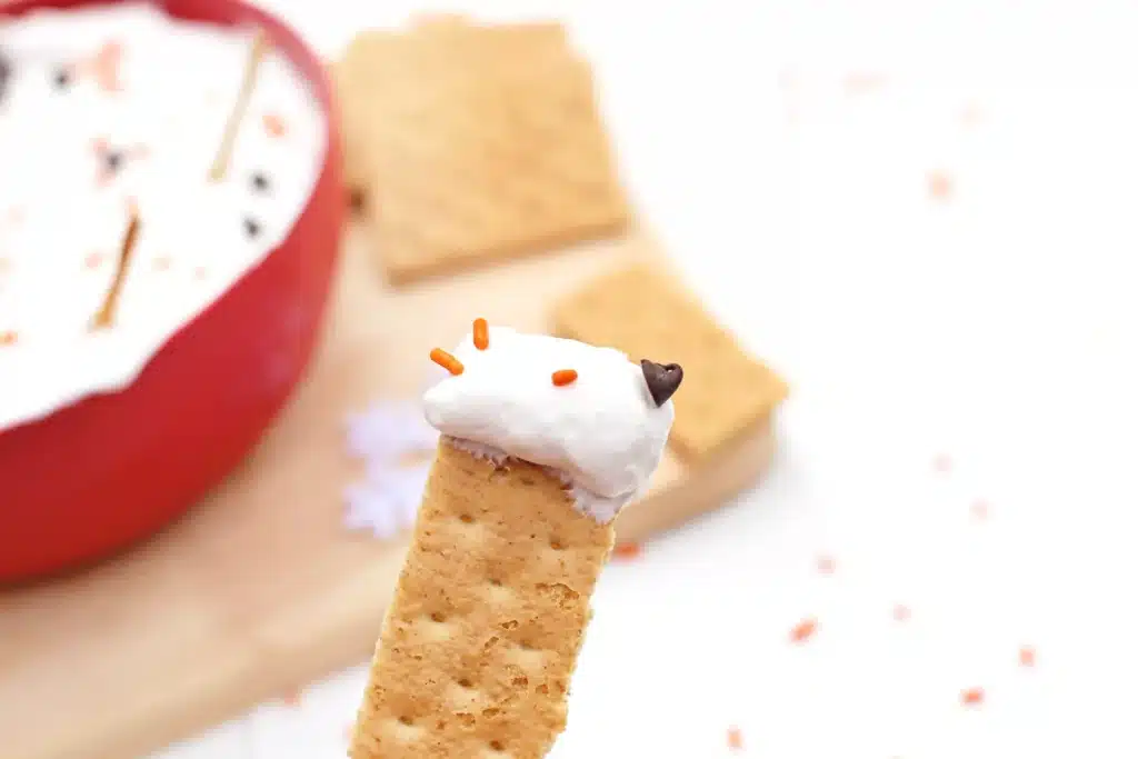 Melted Snowman Cheesecake Dip - Cultivating Brilliant Minds a cracker with the cheesecake dip on it
