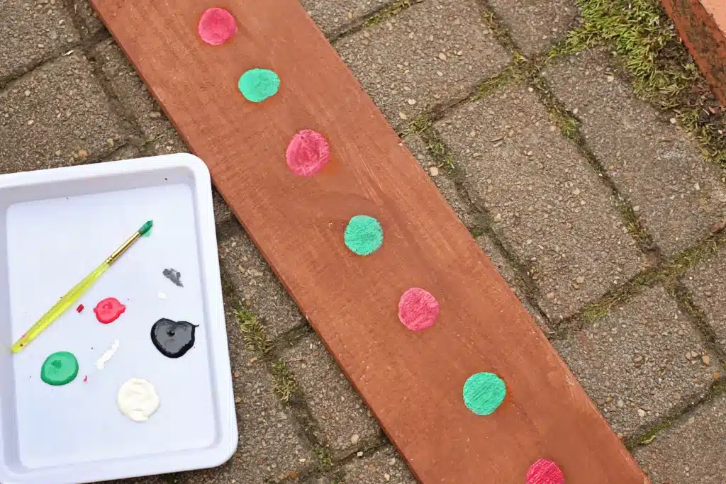 Wooden Gingerbread Keepsake Craft - Cultivating Brilliant Minds a wooden board painted brown with red and green circles in a line