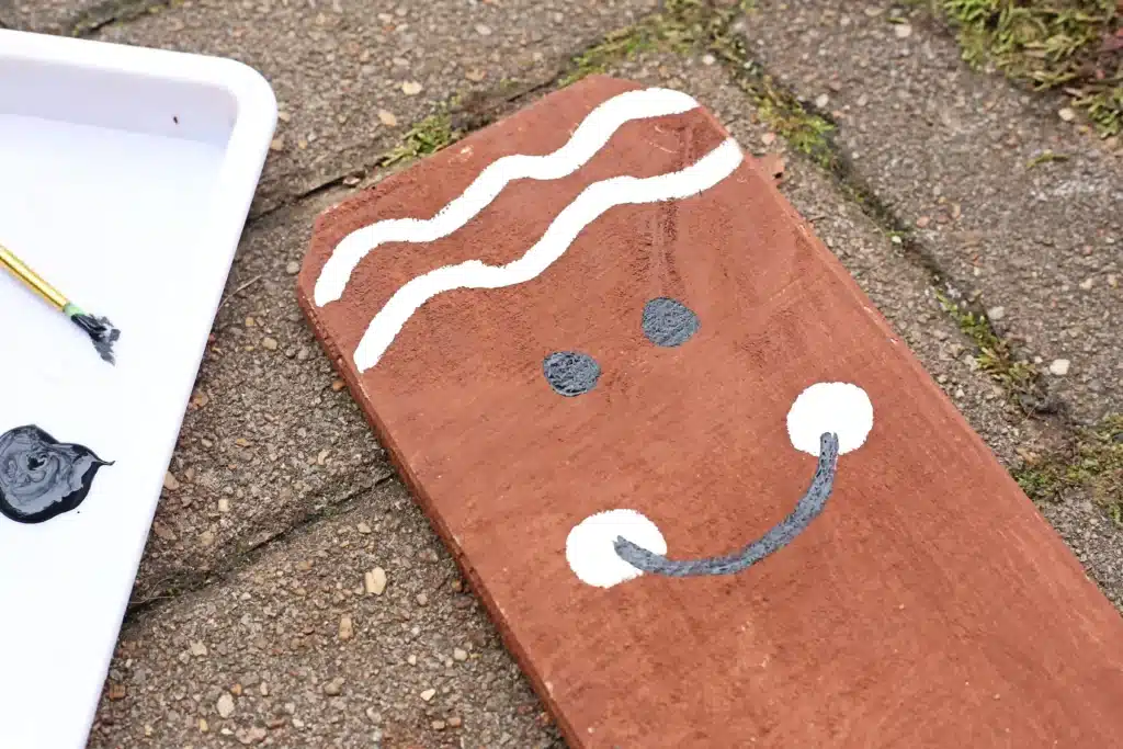 Wooden Gingerbread Keepsake Craft - Cultivating Brilliant Minds a wooden board painted brown with wavy lines for icing and a smiling face