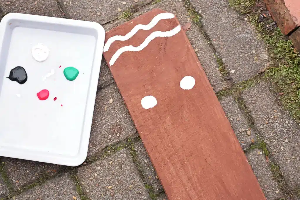 Wooden Gingerbread Keepsake Craft - Cultivating Brilliant Minds a wooden board painted brown with wavy lines for icing and two circles for cheeks