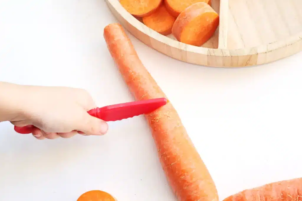 Reindeer Bait Sensory Bin - Cultivating Brilliant Minds a kid cutting a carrot with a red knife