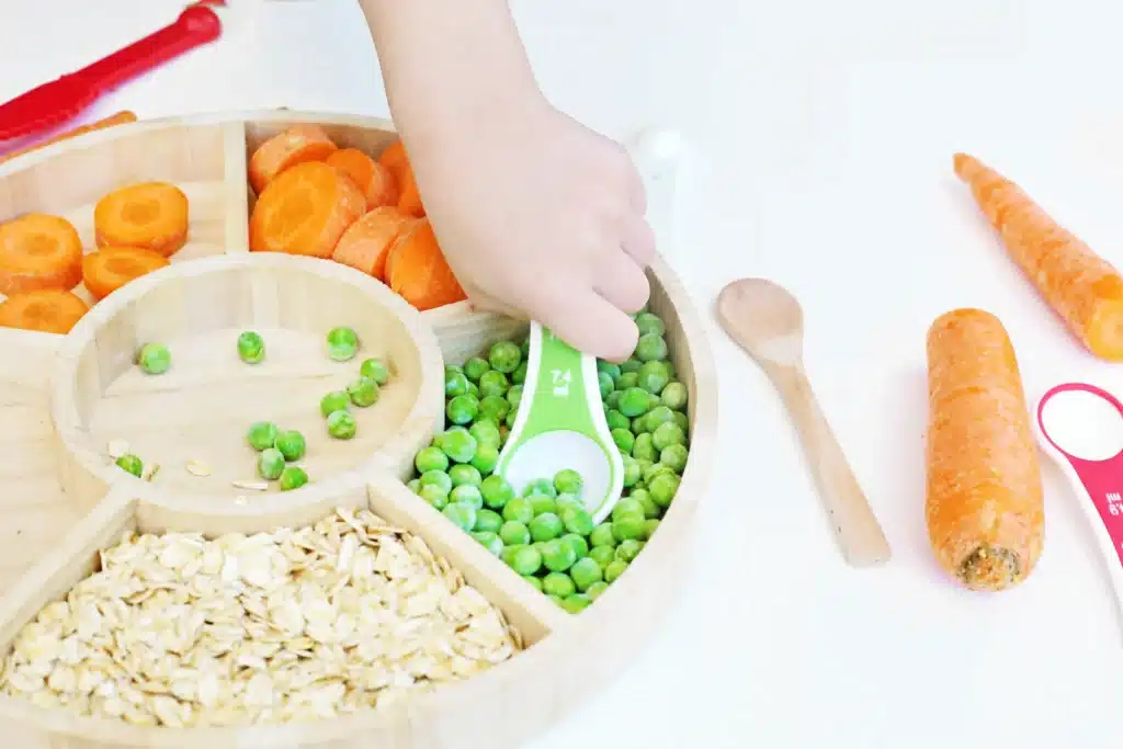 Reindeer Bait Sensory Bin - Cultivating Brilliant Minds a kid scooping up peas