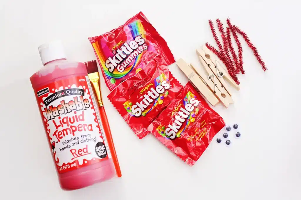 Valentine Candy Love Bugs - Cultivating Brilliant Minds red paint, paint brush, bags of skittles, clothespins, googly eyes, and pipe cleaners