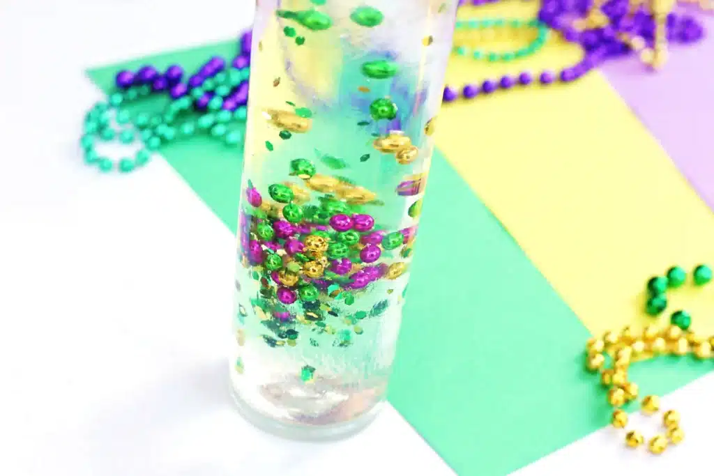Mardi Gras Sensory Bottle - Cultivating Brilliant Minds a water bottle filled with glue, water, glitter, and mardi gras beads