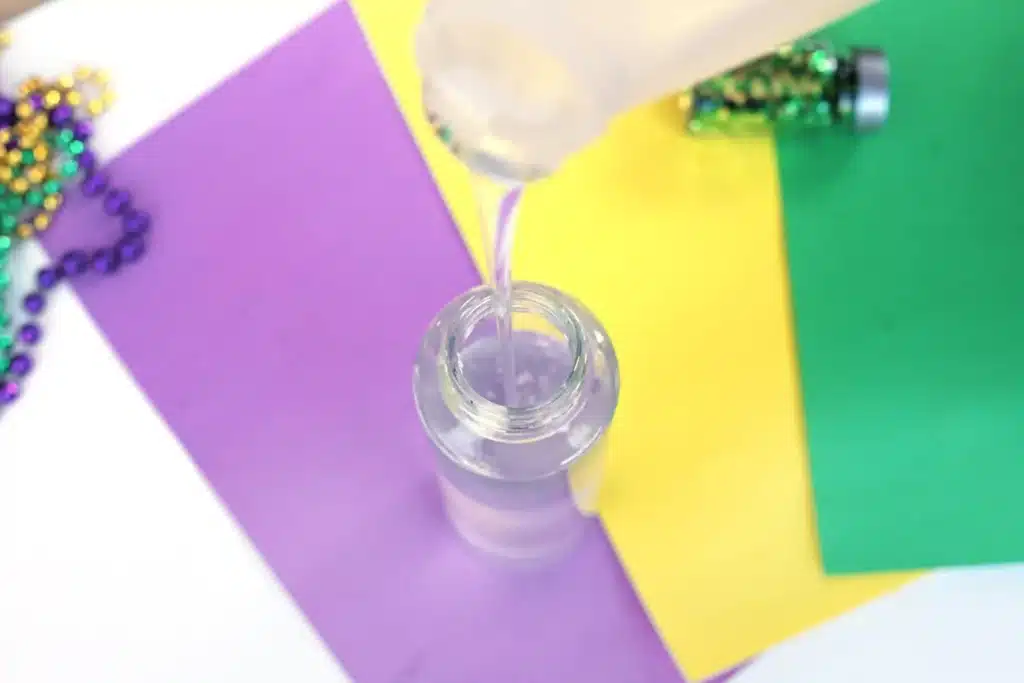Mardi Gras Sensory Bottle - Cultivating Brilliant Minds pouring glue into the empty water bottle
