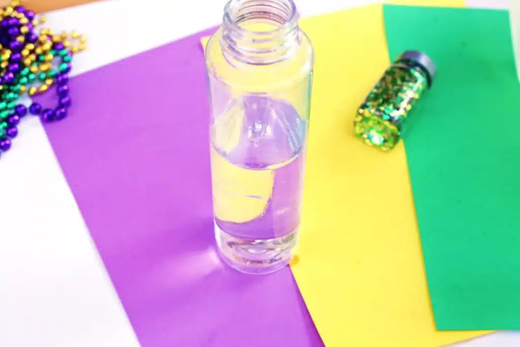 Mardi Gras Sensory Bottle - Cultivating Brilliant Minds a water bottle filled halfway with water
