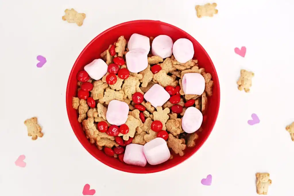 Valentine's Day Cupid Snack Mix - Cultivating Brilliant Minds a red bowl with snack mix inside - pink marshmallows, red m&ms and teddy grahams