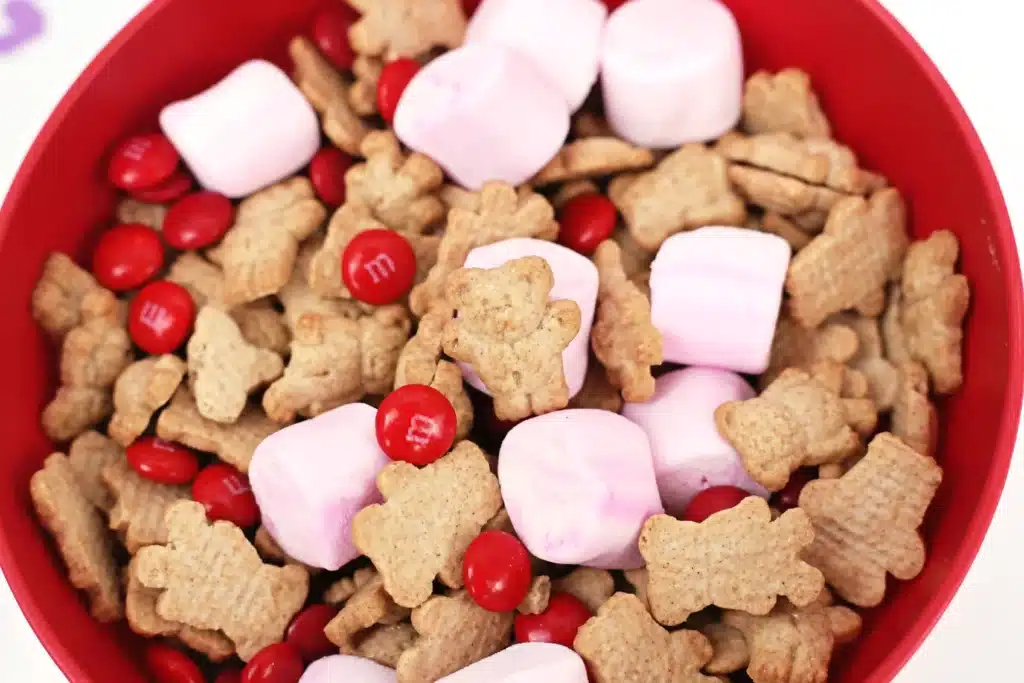 Valentine's Day Cupid Snack Mix - Cultivating Brilliant Minds a red bowl with snack mix inside - pink marshmallows, red m&ms and teddy grahams