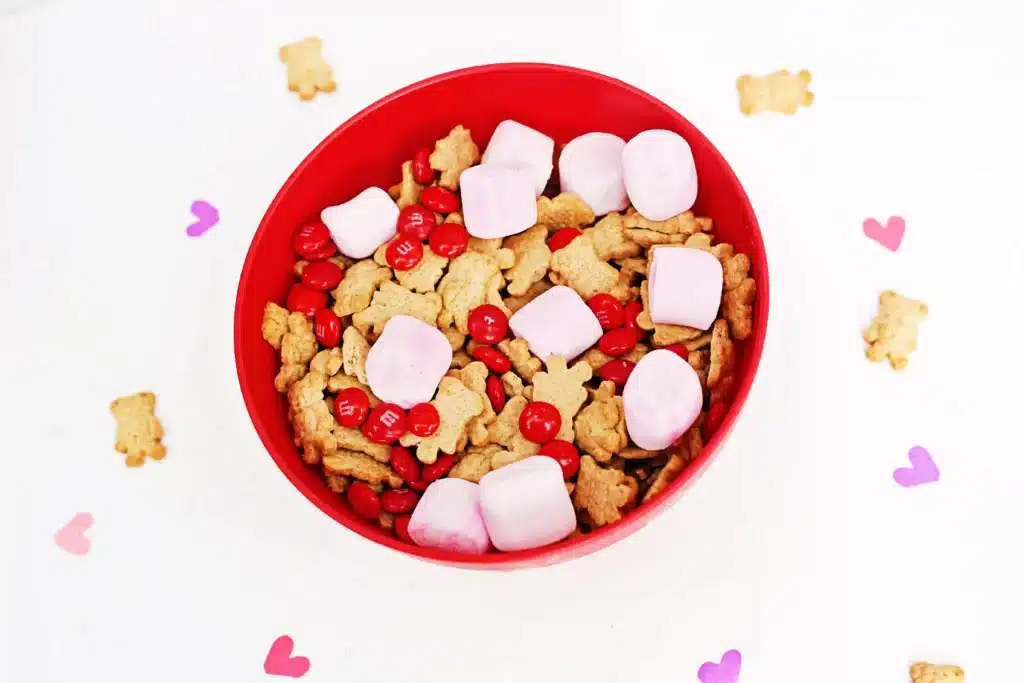 Valentine's Day Cupid Snack Mix - Cultivating Brilliant Minds a red bowl with snack mix inside - pink marshmallows, red m&ms and teddy grahams