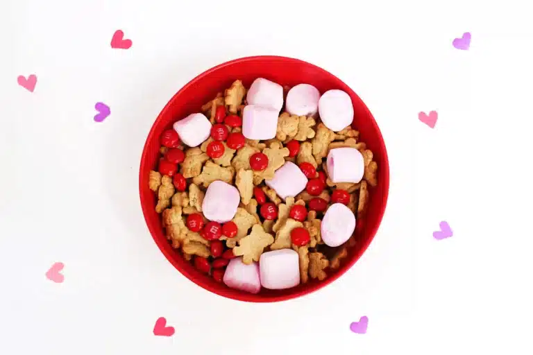 a red bowl with snack mix inside - pink marshmallows, red m&ms and teddy grahams