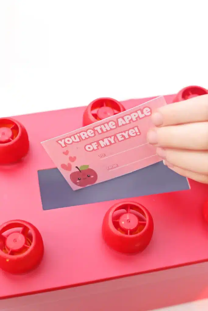 DIY LEGO Valentine Box - Cultivating Brilliant Minds a kid placing a valentine inside a valentine box decorated to look like a lego