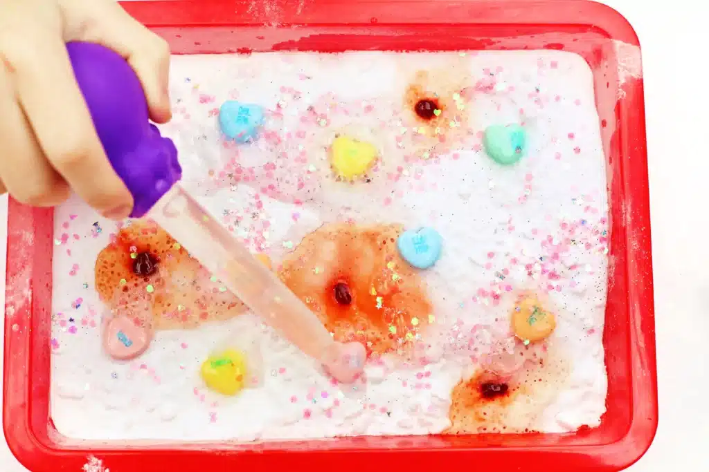 Valentine's Day Fizzy Candy Hearts Experiment - Cultivating Brilliant Minds valentine's day stem activity with a kid using a pipette to pour vinegar over candy hearts with baking soda on them