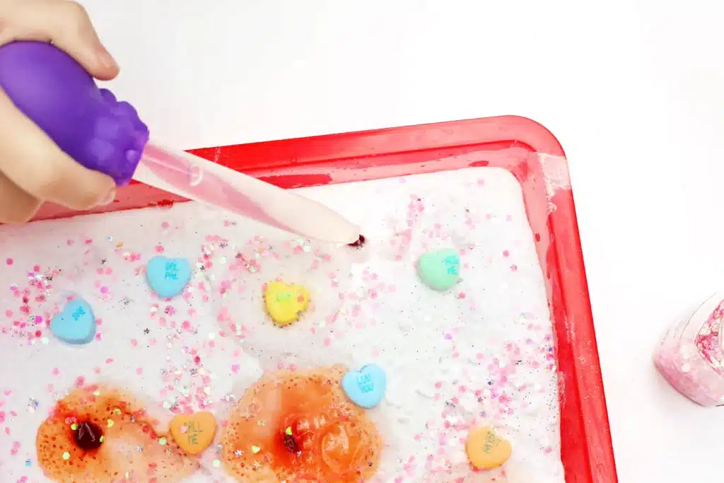Valentine's Day Fizzy Candy Hearts Experiment - Cultivating Brilliant Minds valentine's day stem activity with a kid using a pipette to pour vinegar over candy hearts with baking soda on them