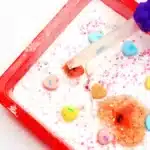 Valentine's Day Fizzy Candy Hearts Experiment - Cultivating Brilliant Minds valentine's day stem activity with a kid using a pipette to pour vinegar over candy hearts with baking soda on them