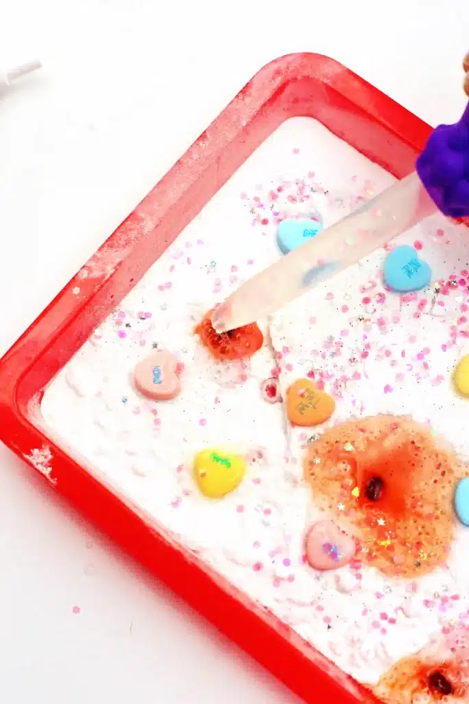 Valentine's Day Fizzy Candy Hearts Experiment - Cultivating Brilliant Minds valentine's day stem activity with a kid using a pipette to pour vinegar over candy hearts with baking soda on them