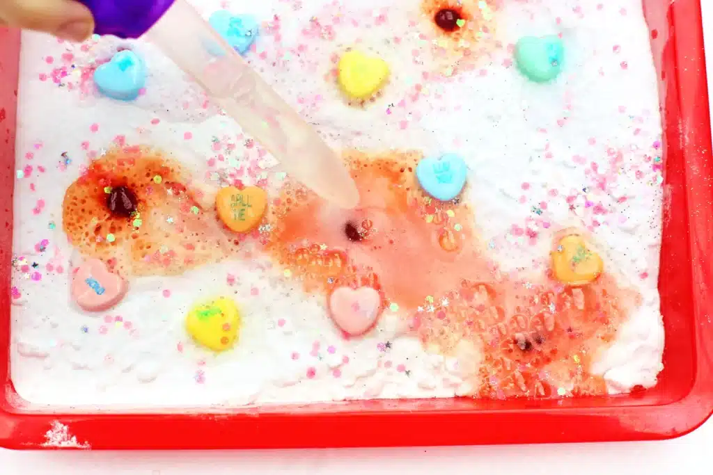 Valentine's Day Fizzy Candy Hearts Experiment - Cultivating Brilliant Minds valentine's day stem activity with a kid using a pipette to pour vinegar over candy hearts with baking soda on them
