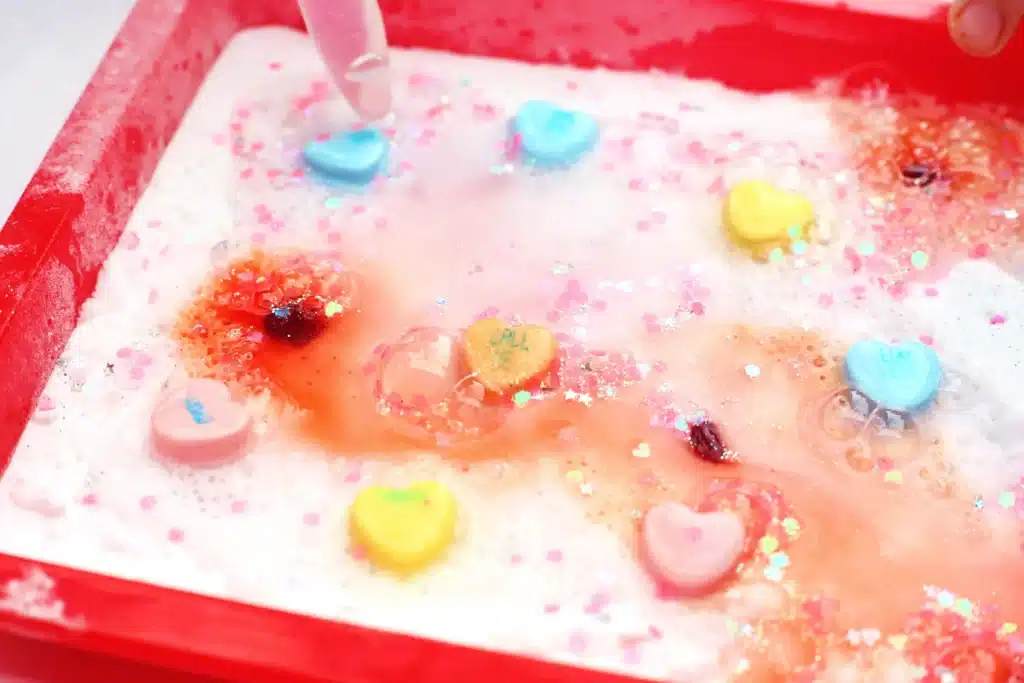 Valentine's Day Fizzy Candy Hearts Experiment - Cultivating Brilliant Minds valentine's day stem activity with a kid using a pipette to pour vinegar over candy hearts with baking soda on them