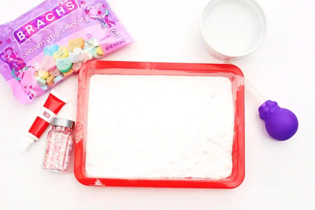Valentine's Day Fizzy Candy Hearts Experiment - Cultivating Brilliant Minds a tray, baking soda, vinegar, red food dye, a pipette, and water