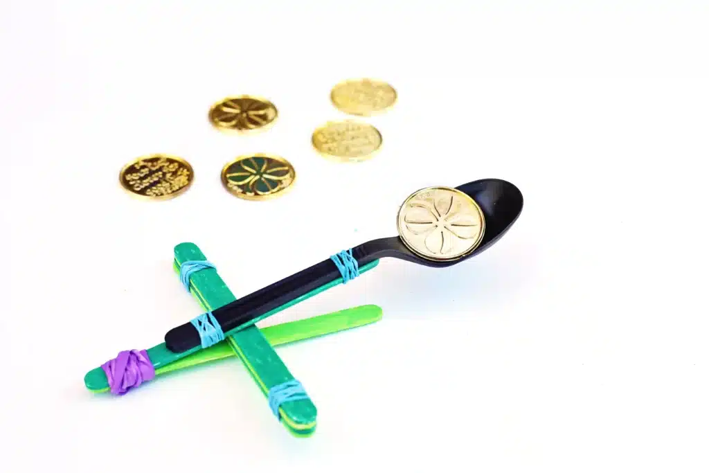 St. Patrick's Day Gold Coin Catapults - Cultivating Brilliant Minds a spoon attached to popsicle sticks with rubber bands to make a catapult