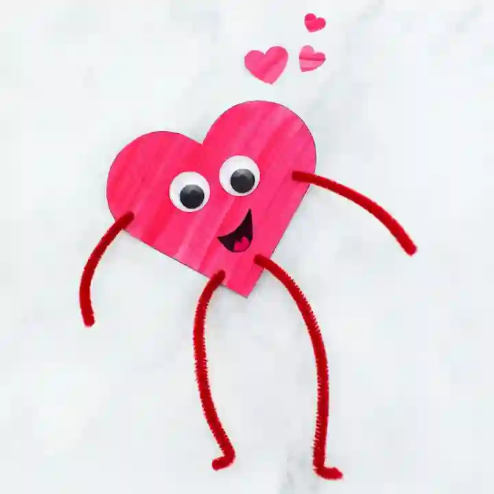 Heart-Themed Crafts For Kids This Valentine's Day - Cultivating Brilliant Minds a piece of paper cut into a heart with a face on it. Pipe cleaners are added to look like arms and legs