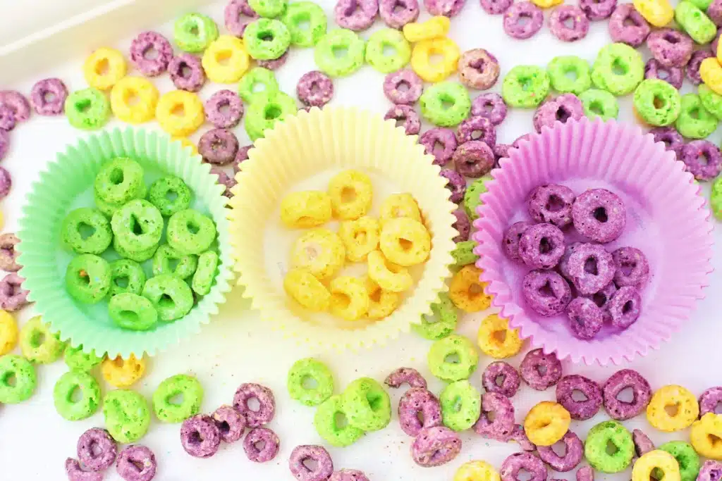 Mardi Gras Color Sorting Sensory Bin - Cultivating Brilliant Minds green, yellow, and purple froot loops separated by color in the corresponding color muffin liner