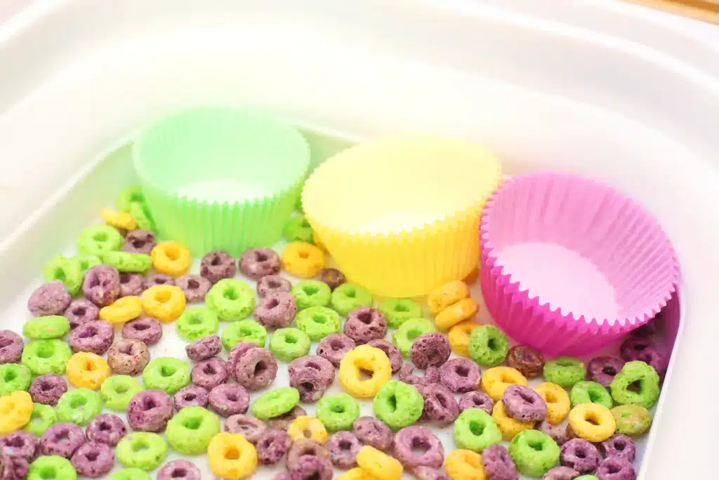 Mardi Gras Color Sorting Sensory Bin - Cultivating Brilliant Minds green, yellow, and purple froot loops next to green, yellow, and purple muffin tin liners
