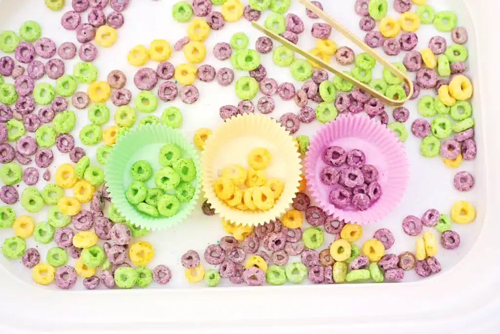 Mardi Gras Color Sorting Sensory Bin - Cultivating Brilliant Minds green, yellow, and purple froot loops separated by color in the corresponding color muffin liner