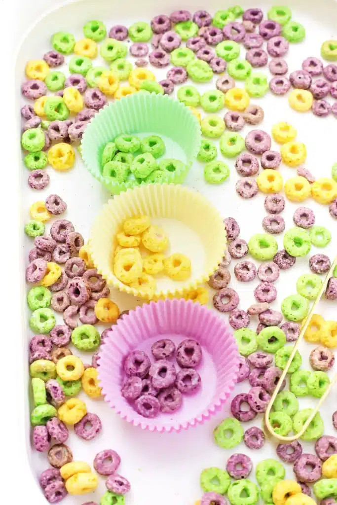 Mardi Gras Color Sorting Sensory Bin - Cultivating Brilliant Minds green, yellow, and purple froot loops separated by color in the corresponding color muffin liner