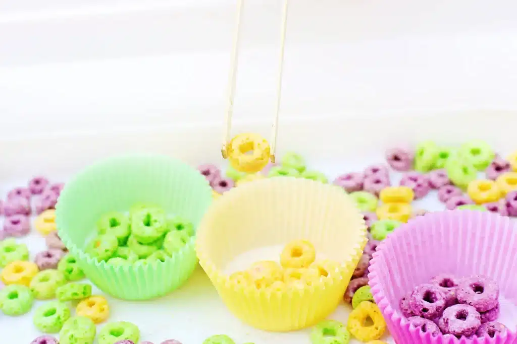 Mardi Gras Color Sorting Sensory Bin - Cultivating Brilliant Minds green, yellow, and purple froot loops separated by color in the corresponding color muffin liner