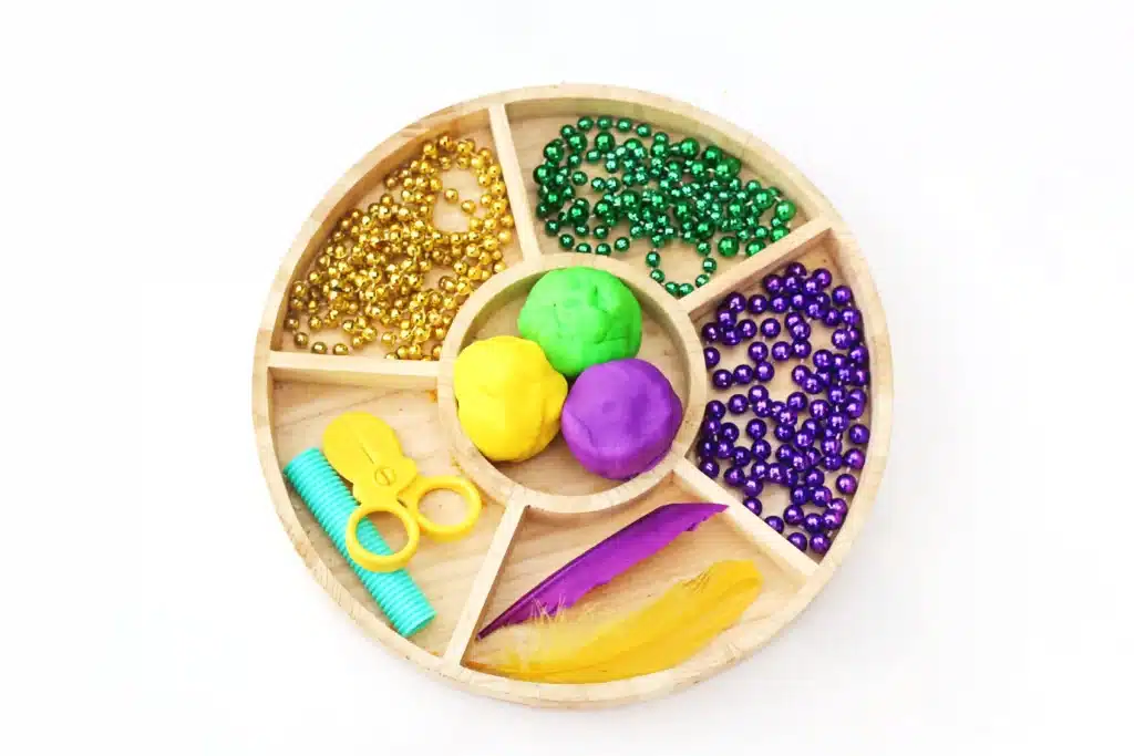 Mardi Gras Playdough Tray 1 - Cultivating Brilliant Minds a tray full of colored playdough, beaded necklaces, feathers, and plastic scissors