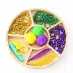 Mardi Gras Playdough Tray 1 - Cultivating Brilliant Minds a tray full of colored playdough, beaded necklaces, feathers, and plastic scissors