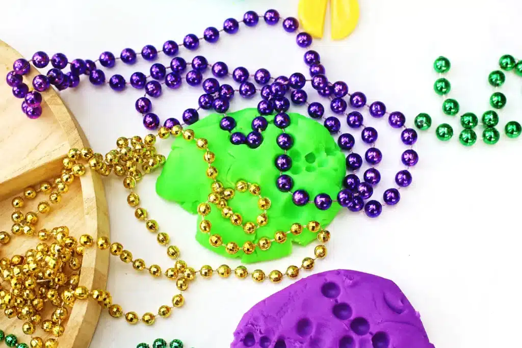 Mardi Gras Playdough Tray - Cultivating Brilliant Minds colored playdough with beaded necklaces on top