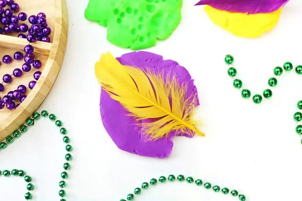 Mardi Gras Playdough Tray - Cultivating Brilliant Minds a feather pressed into purple playdough