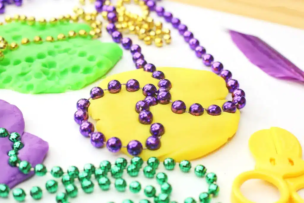 Mardi Gras Playdough Tray - Cultivating Brilliant Minds beaded necklaces pressed into playdough