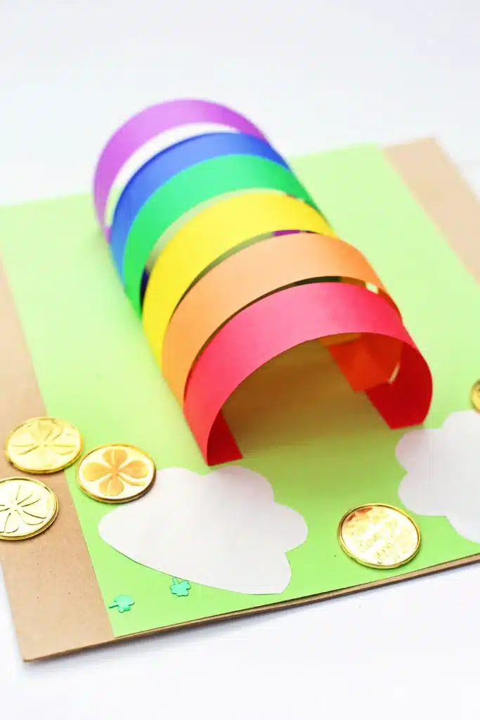 DIY Paper Leprechaun Trap STEM Craft - Cultivating Brilliant Minds colored construction paper glued to a piece of green paper. The colored construction paper is glued as an arch to catch a leprechaun. There are gold coins around it.