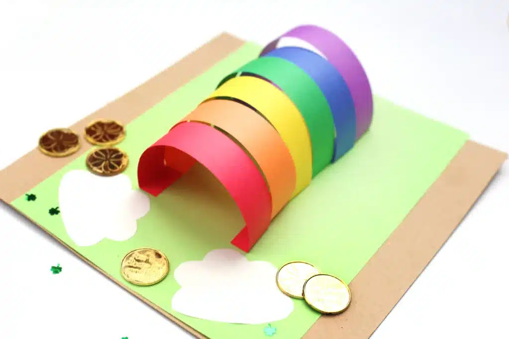 DIY Paper Leprechaun Trap STEM Craft - Cultivating Brilliant Minds colored construction paper glued to a piece of green paper. The colored construction paper is glued as an arch to catch a leprechaun. There are gold coins around it.