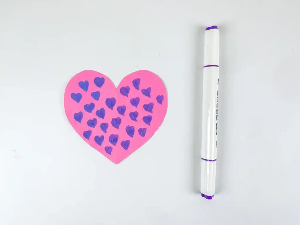 Lovebird Paper Plate Craft for Valentine's Day - Cultivating Brilliant Minds a piece of pink construction paper cut into a heart with drawn hearts all over it