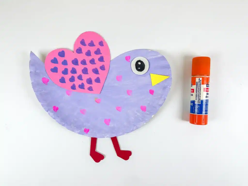 Lovebird Paper Plate Craft for Valentine's Day - Cultivating Brilliant Minds a paper plate cut and colored to look like a lovebird. It is painted purple with pink hearts and has a pink heart with purple hearts drawn all over it for a wing.