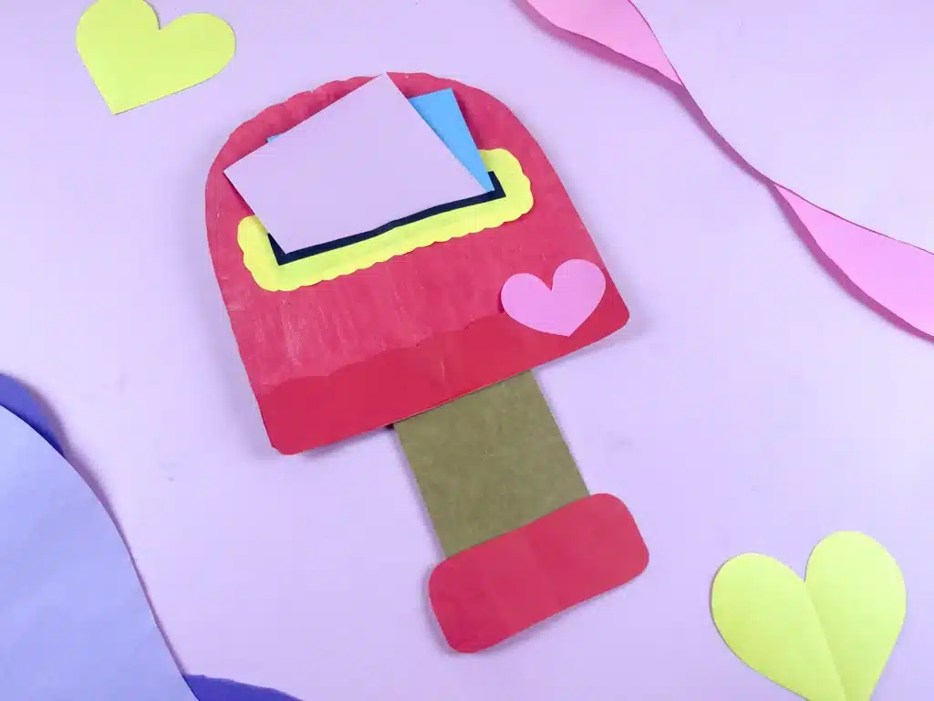 Valentine's Day Mailbox Paper Plate Craft - Cultivating Brilliant Minds a paper plate painted pink and cut into the shape of a mailbox with a slot cut in the middle for mail.