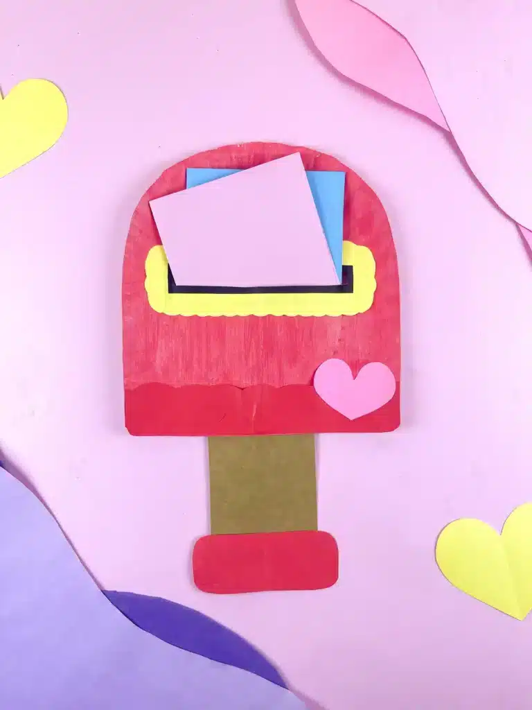 Valentine's Day Mailbox Paper Plate Craft - Cultivating Brilliant Minds a paper plate painted pink and cut into the shape of a mailbox with a slot cut in the middle for mail.