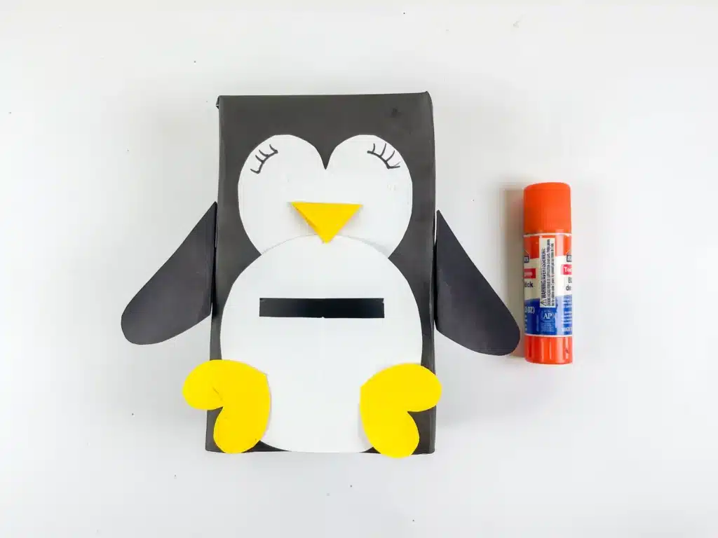 Penguin Valentine Box - Cultivating Brilliant Minds a box covered in black paper with white construction paper on top to look like the penguin's body, black construction paper flippers, and yellow construction paper for the beak and feet