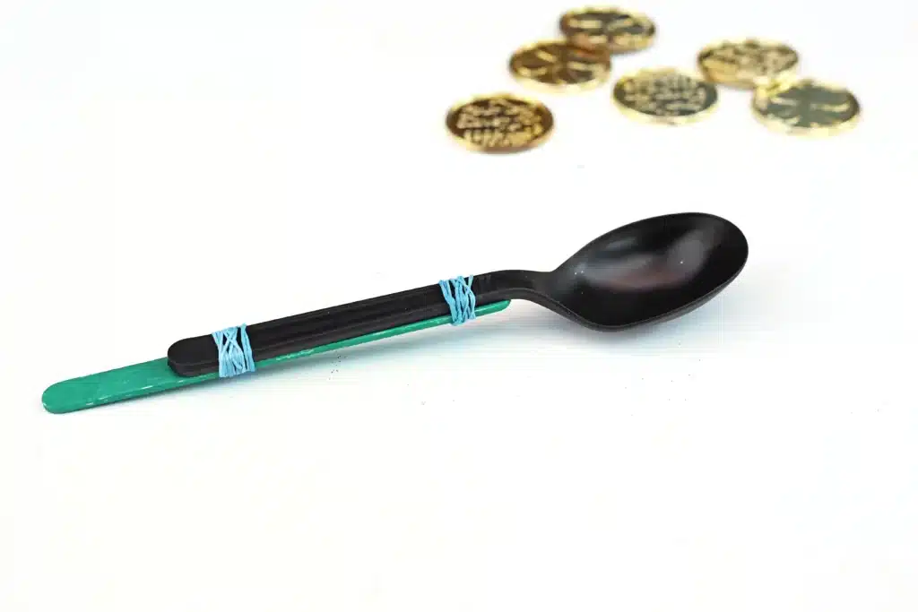 St. Patrick's Day Gold Coin Catapults - Cultivating Brilliant Minds a popsicle stick attached to a spoon with rubber bands