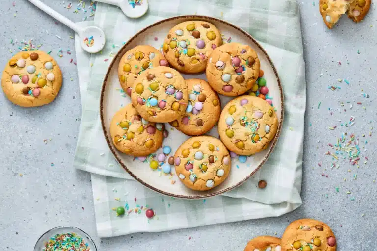 chewy cookies with easter colored pastel m&ms on a white plate on top of a light green plaid tea towel