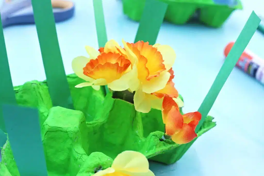 Easter Egg Garden Craft - Cultivating Brilliant Minds an egg carton painted green with strips of green paper and fake flowers glued in it