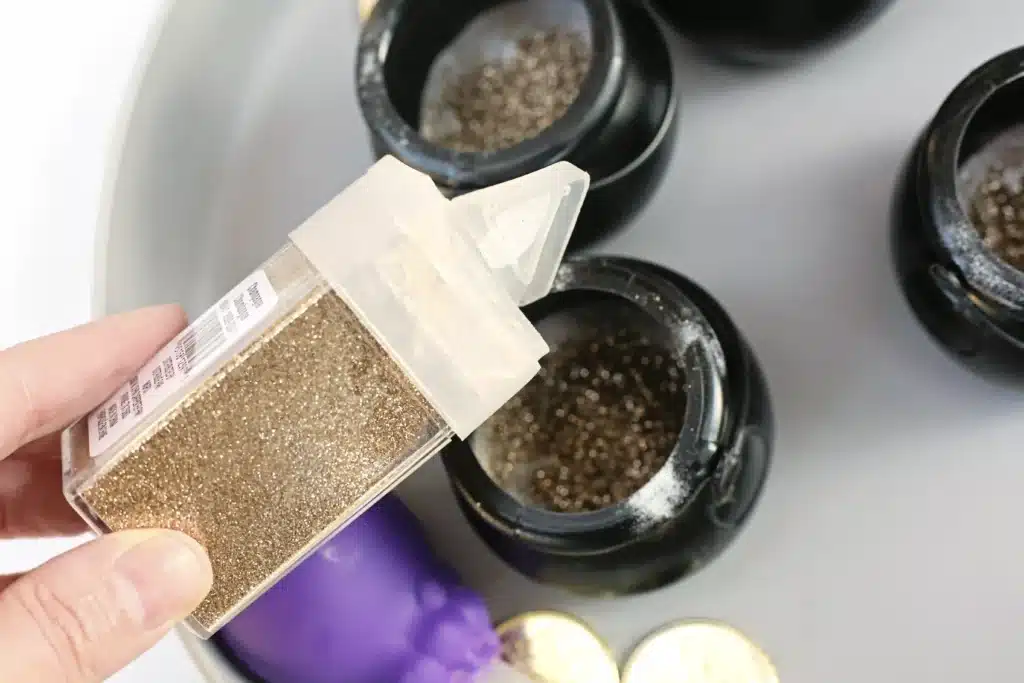 Fizzy Pot of Gold Experiment - Cultivating Brilliant Minds a hand pouring gold glitter into the black cauldron of baking soda