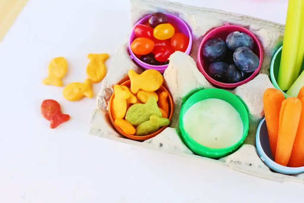 Easter Egg Snack Tray - Cultivating Brilliant Minds an easter egg snack tray with an egg carton with plastic eggs inside and the eggs have jelly beans, blueberries, celery, carrots, goldfish, and ranch dressing inside
