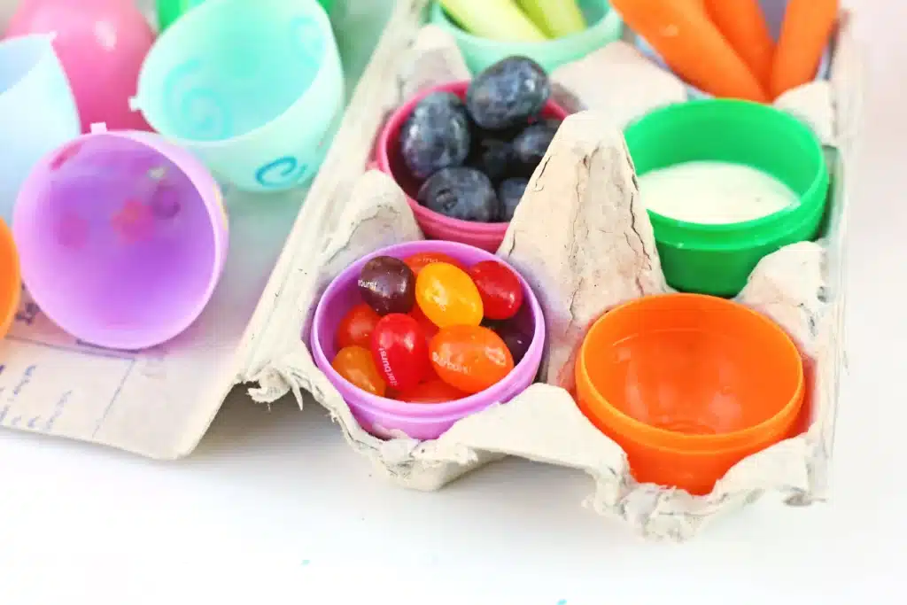 Easter Egg Snack Tray - Cultivating Brilliant Minds an egg carton with plastic eggs inside. the eggs have jellybeans, blueberries, ranch, carrots, and celery in them