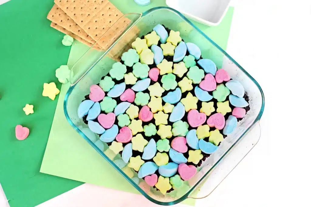 Lucky Charms S'mores Dip - Cultivating Brilliant Minds a baking pan that has chocolate chips layered on the bottom and lucky charms marshmallows on top