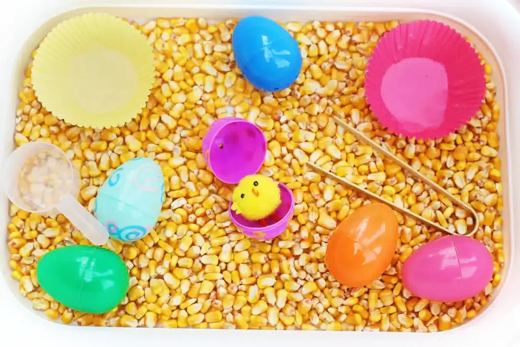 Chick Hatch Sensory Bin - Cultivating Brilliant Minds a chick hatch sensory bin with corn kernels, easter eggs, and chicks