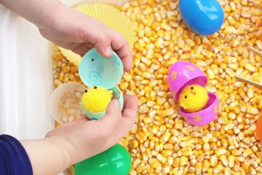 Chick Hatch Sensory Bin - Cultivating Brilliant Minds a kid opening a plastic easter egg that has a chick inside